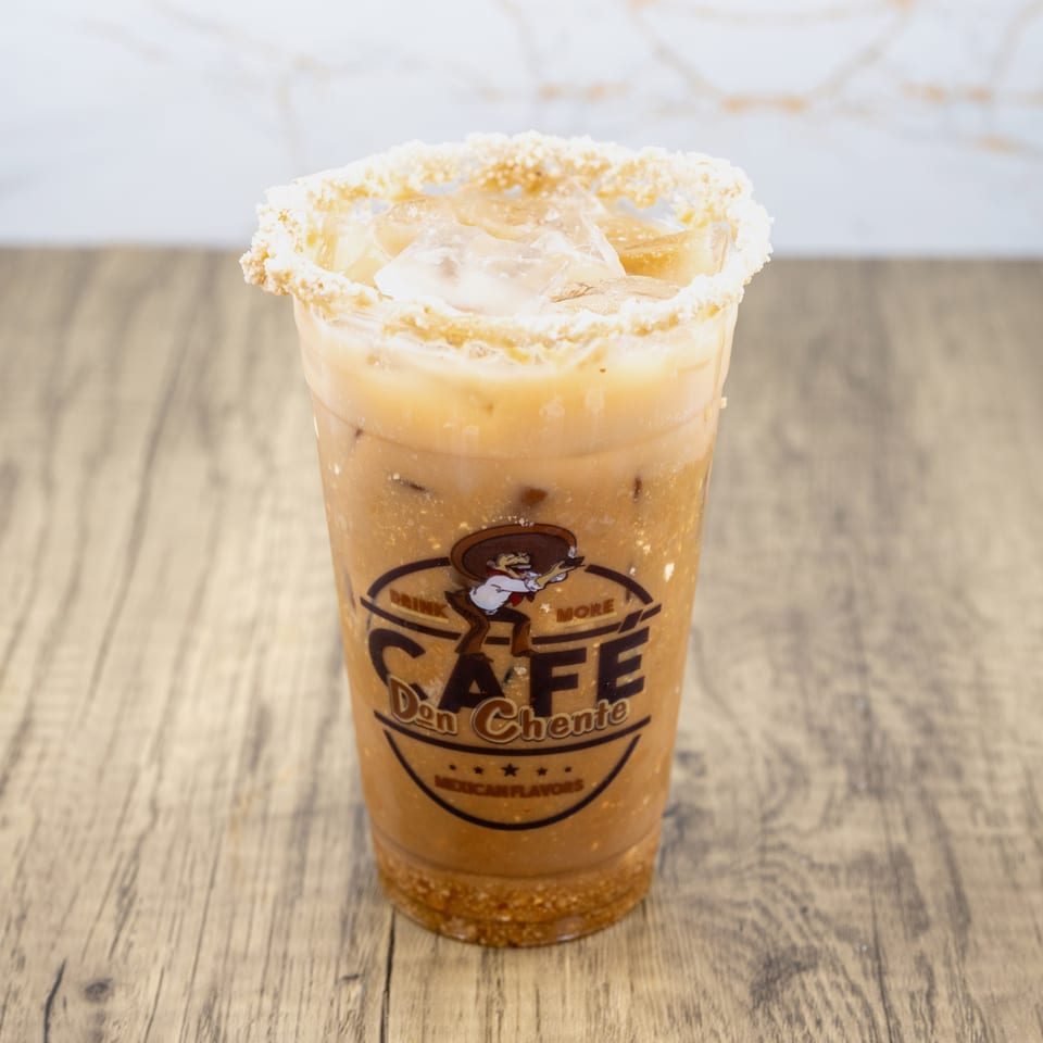 Iced horchata with a crushed cookie rim and Cafe Don Chente logo on a wooden table.