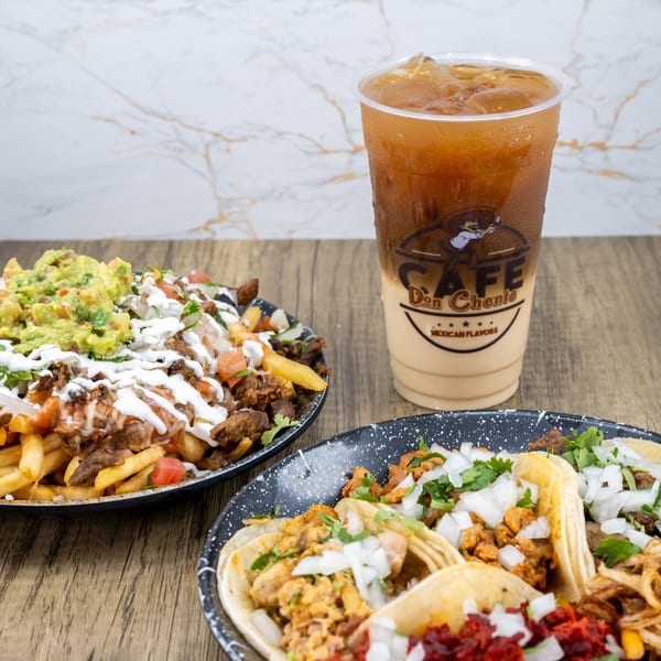 Plates of loaded carne asada fries, assorted tacos, and an iced coffee drink on a wooden table.