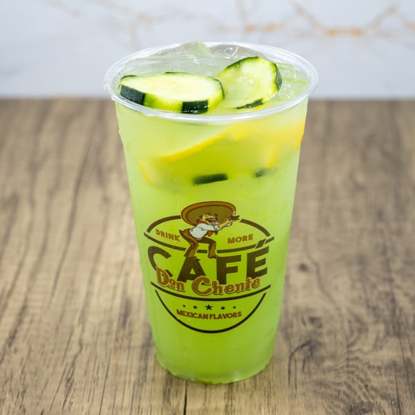 A Cafe Don Chente Mexican Flavors drink, light green with cucumber slices and ice, on a wooden table.