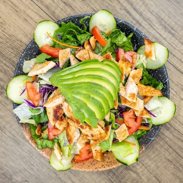 Overhead view of a fresh salad with grilled chicken, sliced avocado, tomatoes, and cucumbers.